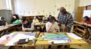 Obiora Udechukwu helps a Saint Lawrence student working on an art project. Several students are busy working on their own projects in the background.