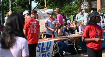 A group of students and faculty members sit and stand behind tables at the Student Organization Fair.