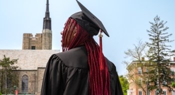Sarath Novas, wearing graduation regalia, gazes off into the distance. Gunnison Memorial Chapel is in the background.