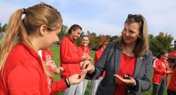 President Morris hands lady bug bracelets to smiling members of the Saints Women's Cross Country Team.