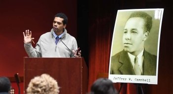 Steve Peraza stands at a podium while delivering a talk next to a large, blown-up yearbook image of Jeffrey Campbell.