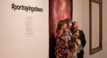 A group of people stand in front of a large painting in the Richard F. Brush art gallery.