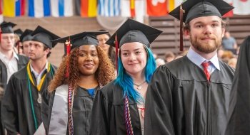 Photo of multiple students smiling as they stand in the processional line at commencment 2024.