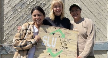 Photo of 3 female students holding a cardboard painted sign that reads &quot;SLU Close the Loop&quot; with a large recycle triangle around the words.