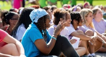 A group of students sitting outside on a sunny day, smiling and clapping during an event at Saint Lawrence University.