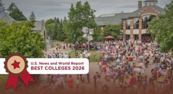 A Large crowd of students and community members gathered outdoors at St. Lawrence University’s campus, surrounded by trees and academic buildings. Booths and tables line the walkway during a vibrant campus event. A U.S. News and World Report “Best Colleges 2026” badge is displayed in the foreground of the image.