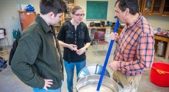 Joe Erilichman and two Saint Lawrence students stand around a large silver bucket brewing beer.