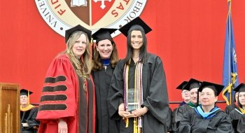 President Kate Morris, Jennifer Curley Reichert and a student stand together, wearing regalia, on the Commencement stage.