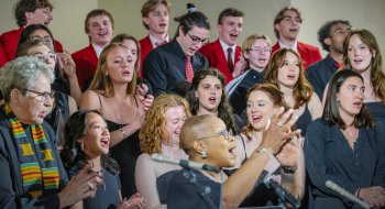 A diverse group of students and a conductor perform together in a choir, singing enthusiastically.