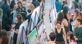 Students presenting research posters at a crowded campus event.