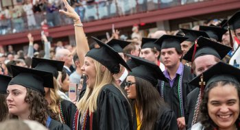 Graduates in caps and gowns celebrate during a commencement ceremony in a crowded arena.