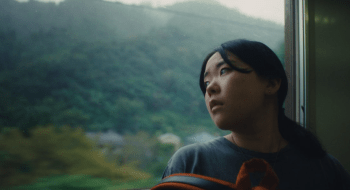 Film still from Chronicle of a City showing a woman looking out a train window.