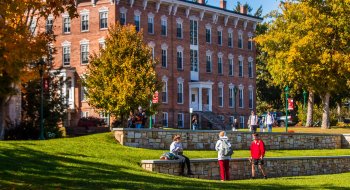 Saint Lawrence students walk about the quad on a sunny fall day. There are bright orange and red leaves scattered on the ground.