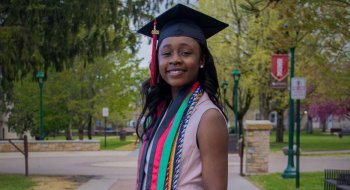 Francesca Mnenula wearing a graduation cap and cords on a college campus.