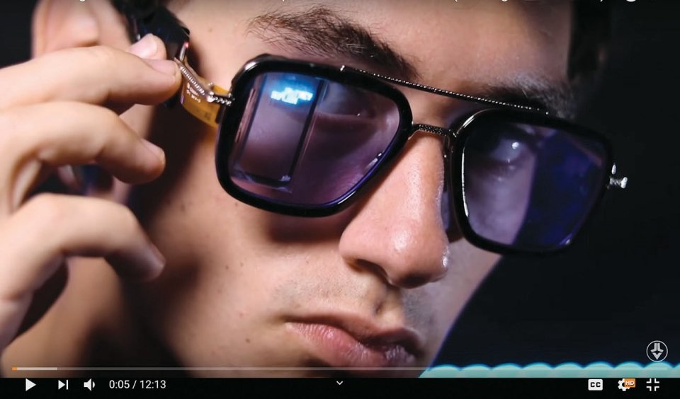 A screenshot of a YouTube video featuring Jake Laser's face who is wearing glasses that reflect a phone screen in them.