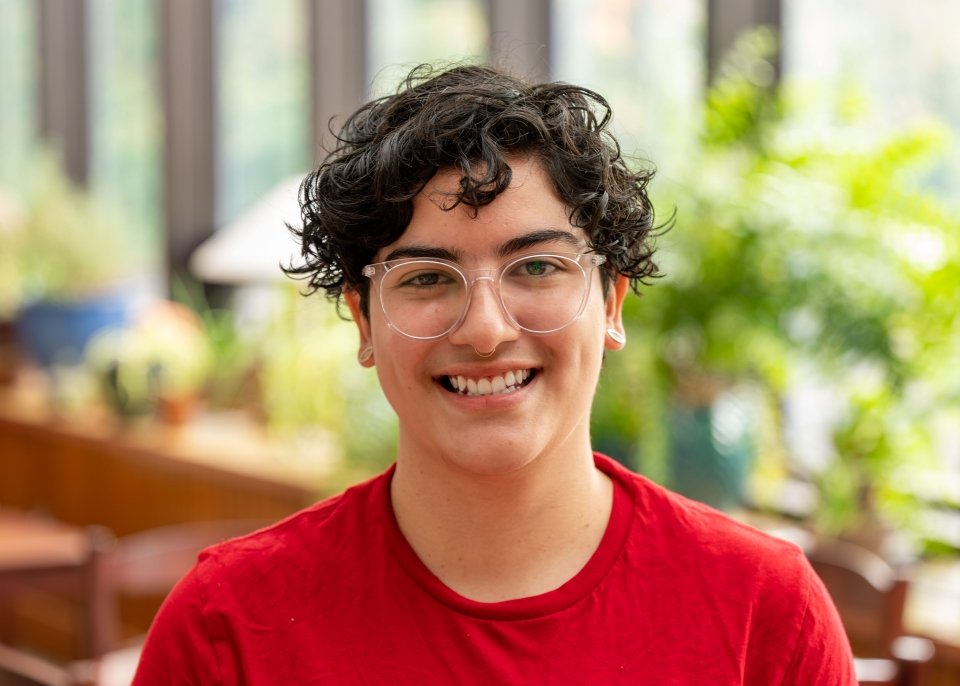 Headshot of Alejandra, with short, dark curly hair, light glasses, and a red t-shirt on.