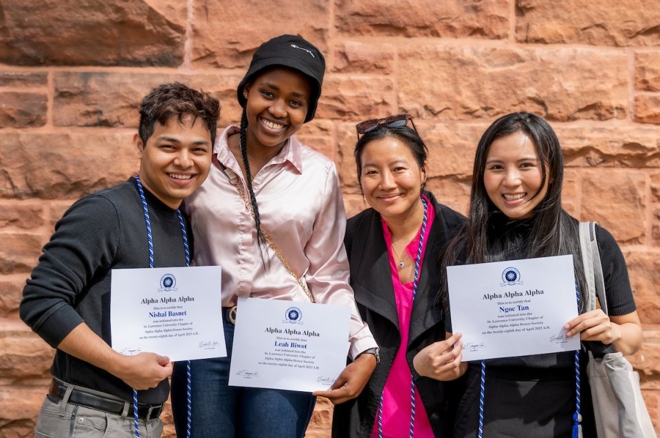 Four new members of the Alpha Alpha Alpha honor society stand smiling with certificates of recognition.