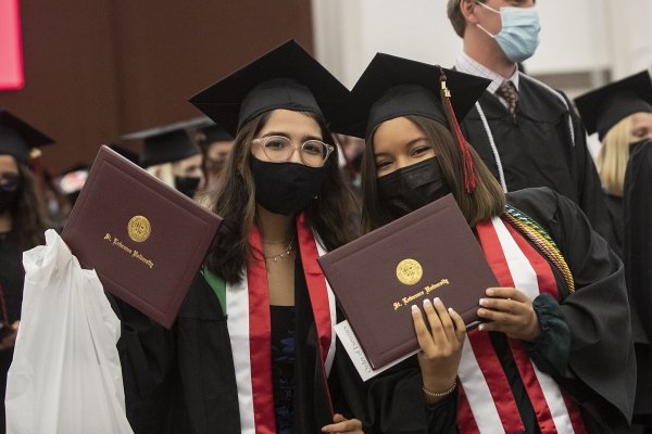 Two graduates hold up their diploma covers for the camera after Commencement.