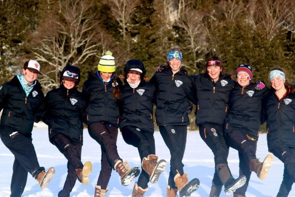 Eight members of the Saint Lawrence Nordic ski team, wearing performance leggings and black jackets, standing in a line with their arms around each other.