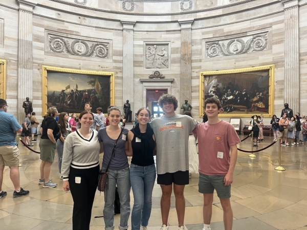Five college-aged men and women with their arms around each other, smiling for a photo while visiting the Rotunda of the U.S. Capitol.