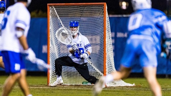 William Helm, wearing a white and blue Duke Lacrosse uniform, defends the lacrosse net as the competition creeps in.