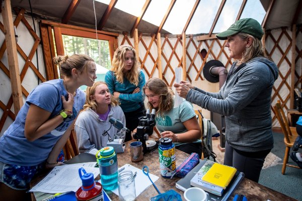 A professor holds up a piece of paper in explanation to a group of students in a yurt.