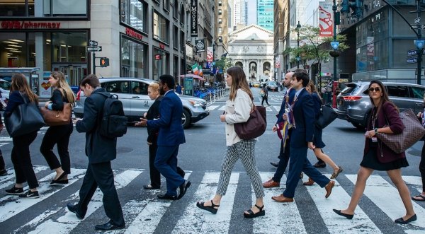 A group of Saint Lawrence students, wearing professional attire, use the crosswalk on a busy street in New York City.