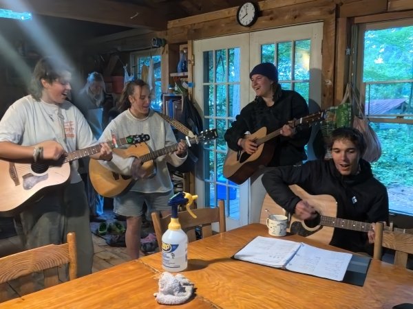 Resident musicians Garen Steiner, Beckley Wooster, Lars Fattinger, and Jacqui Smith playing guitar around the table.