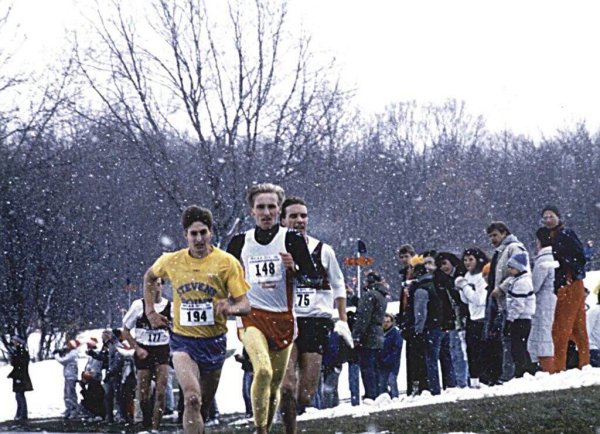 Two runners lead the pack during a distance race on a snowy day.