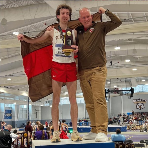 Nick Lyndaker stands next to his couch, holding a trophy and the St. Lawrence flag after winning the national championship.