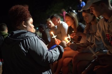 A group of students holding white candles. One turns to two others to help light the candle they're holding.