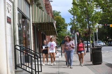 Four students and a professor walk on a main street, lined with shops, on a sunny day in Canton, New York.