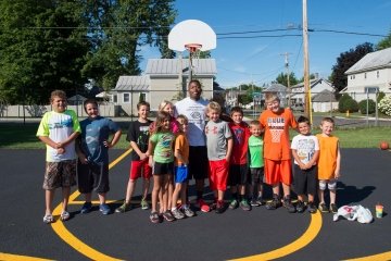 A St. Lawrence student stands with a group of school children on a basketball court.