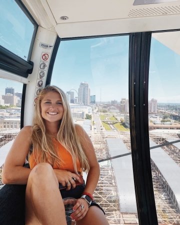 Sydney Giacin sitting in an enclosed, windowed space with a city skyline behind her.