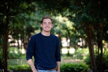 Craig Wilkes '22, wearing a dark blue sweater, stands in a grove of trees. 