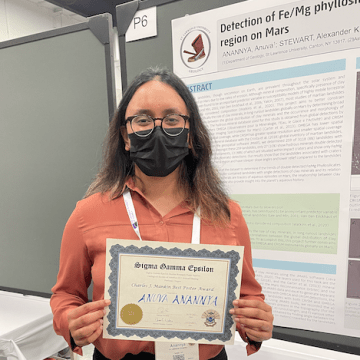 Anuva Anannya holds her award for Best Poster and the annual Geological Society meeting. Her award-winning poster on Mars is in the background. 