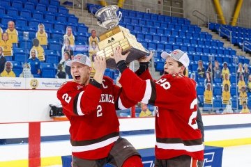 Two men's ice hockey players excitedly hoist a championship trophy they just won.