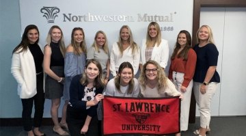 A group of 11 Laurentians stand in front of a Northwestern Mutual sign while holding a Saint Lawrence University banner.
