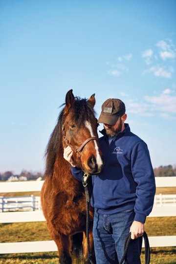 Photo of retired First Sergeant Chad Van Gorder standing alongside a horse, with his hand around its face.