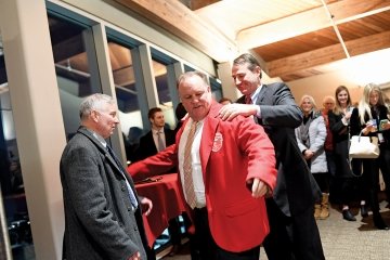 A photo of alumni Peter McGeough having a red blazer placed around his shoulders.