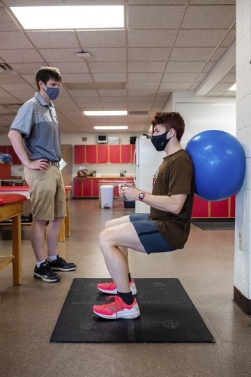 A student working out with a trainer watching
