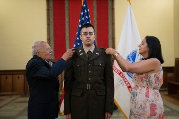 A Reserve Officers Training Corps cadet is flanked by family members who attach patches to his uniform to commemorate their commissioning. 