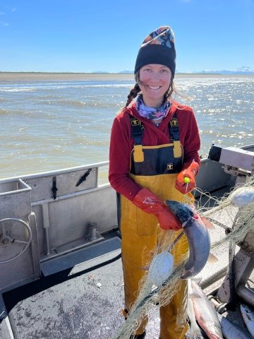 Jessica Normandeau, wearing yellow rubber waders, wrangles a silver salmon out of a net.