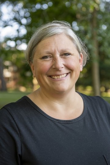 Headshot of Professor Jennifer Thomas. She is standing against a backdrop of trees and wearing a simple black dress.