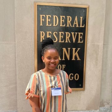 Zenani Mabuza, wearing an orange, cream, and blue striped dress, stands in front of the Federal Reserve Bank of Chicago.