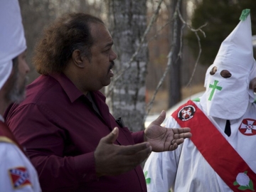 Daryl Davis speaks with a robed and hooded KKK member