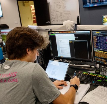 A student sits at a Bloomberg Terminal workstation while writing in the notepad in front of him.