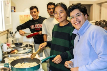 Four smiling Saint Lawrence students cook a meal together in a kitchen.