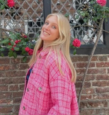 Photo of Lilly Sullivan, wearing a pink plaid oversized jacket and standing in front of a rose trellis.