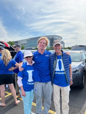 Joan Officer, William Helm, and David Officer, wearing bright blue Duke jerseys, stand together in a parking lot during a tailgate celebration.